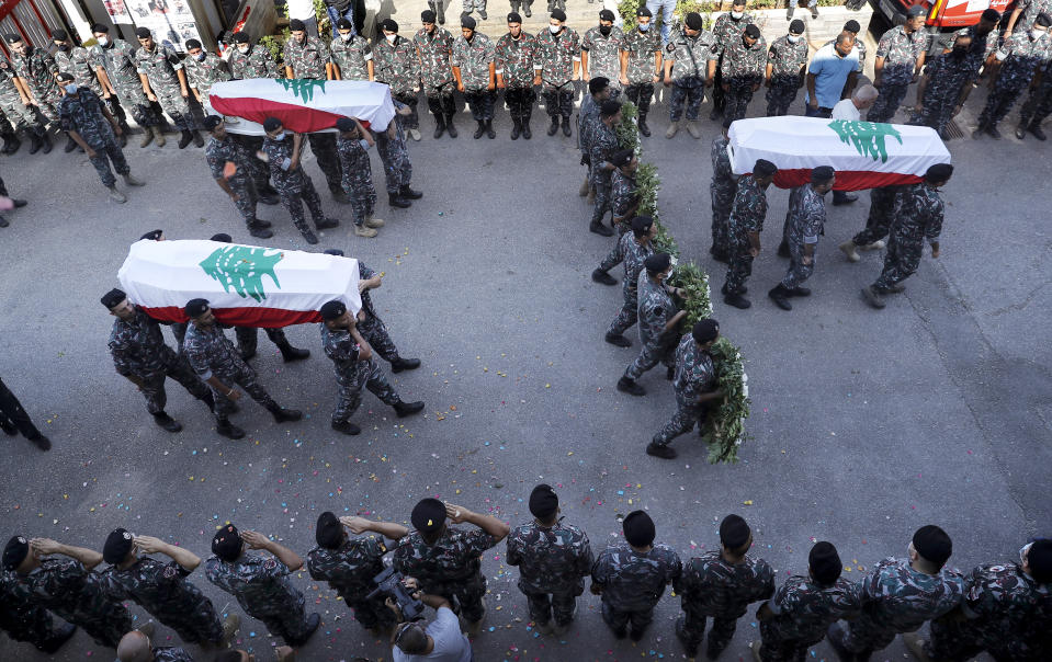 Firefighters carry the coffins of three of their comrades who were killed during the Aug. 4, 2020 explosion that hit the seaport of Beirut while other comrades salute during their funerals at the firefighter headquarters in Beirut, Lebanon, Monday, Aug. 17, 2020. (AP Photo/Hussein Malla)