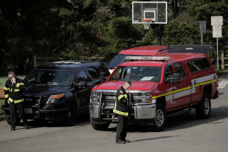 Firefighters talk on the phone near fire and police vehicles in a staging area at the North Kirkland Community Center, which is a short drive from the Life Care Center of Kirkland