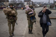 Ukrainian soldiers carry babies helping a fleeing family to find a vehicle after crossing the Irpin river in the outskirts of Kyiv, Ukraine, Saturday, March 5, 2022. (AP Photo/Emilio Morenatti)