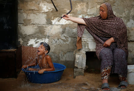 A Palestinian woman bathes her son with water from a tank, filled by a charity, inside their dwelling in Khan Younis, in the southern Gaza Strip, July 3, 2017. REUTERS/Mohammed Salem