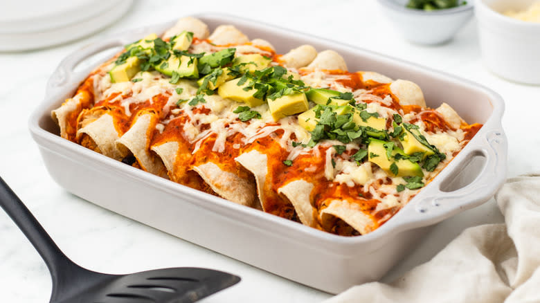 Avocado topped enchiladas in a baking dish