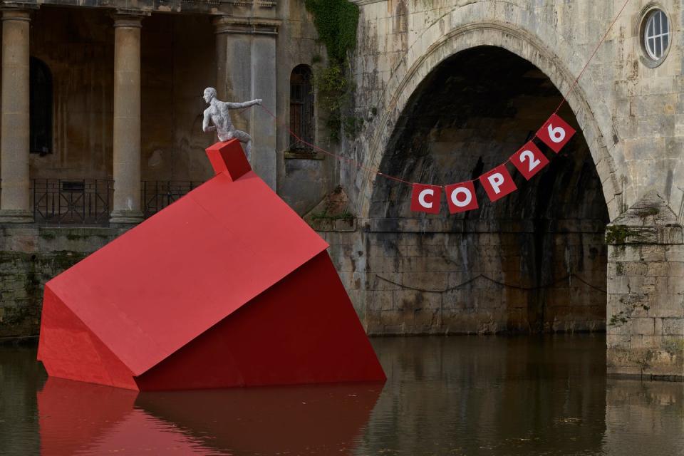 A red house sinks into a lake.