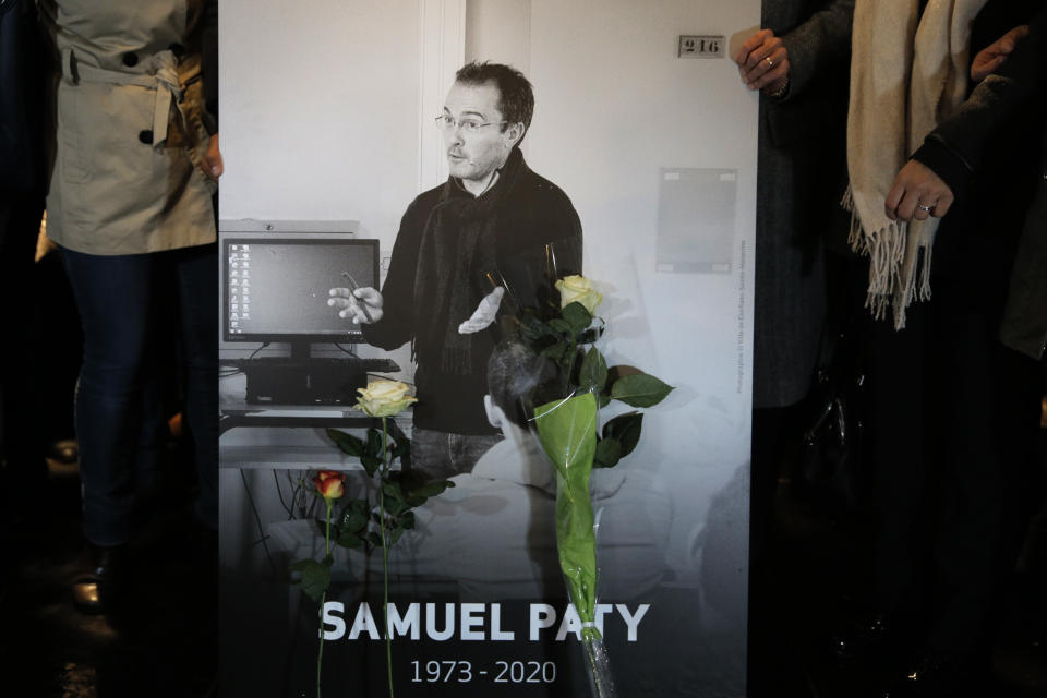 People hold a photo of the history teacher Samuel Paty , who was beheaded last week, during a memorial march in homage to him, Tuesday, Oct.20, 2020 in Conflans-Sainte-Honorine, northwest of Paris. Samuel Paty was beheaded on Friday by an 18-year-old Moscow-born Chechen refugee, who was later shot dead by police. Police officials said Paty had discussed caricatures of Islam's Prophet Muhammad with his class, leading to threats. (AP Photo/Lewis Joly)