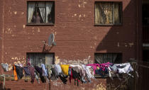 Residents watch through their home window as protesters clash with police in Eldorado Park, Johannesburg, South Africa, Thursday, Aug. 27, 2020. Residents from the township, south of Johannesburg are demanding justice for a teenager shot and killed, allegedly at the hands of police Wednesday. (AP Photo/Themba Hadebe)