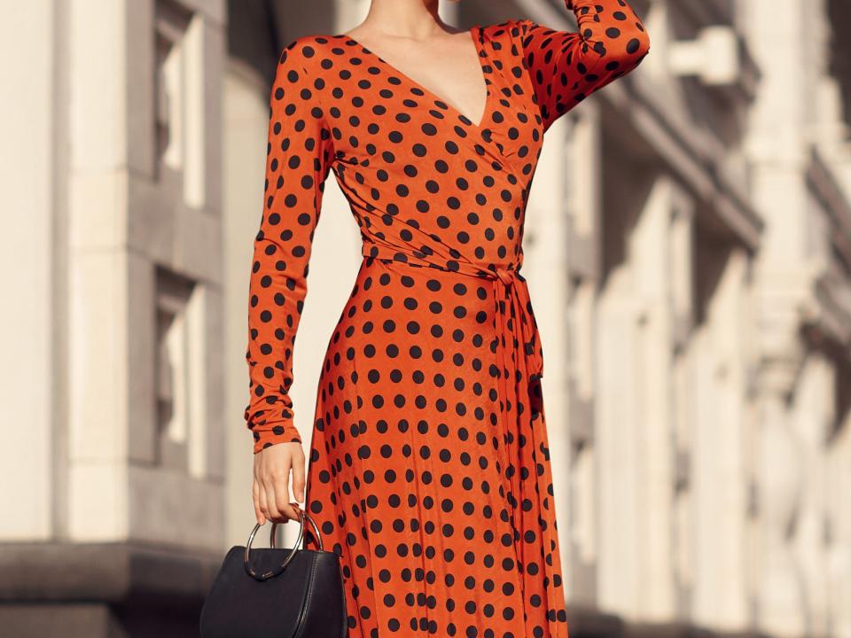 woman wearing a red polka dot dress and lack sunglasses stepping outside