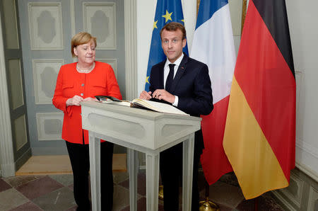 German Chancellor Angela Merkel looks on as French President Emmanuel Macron signs the guest book prior to a bilateral meeting at the German government guesthouse Meseberg Palace in Meseberg, Germany, June 19, 2018. John MacDougall/Pool via REUTERS