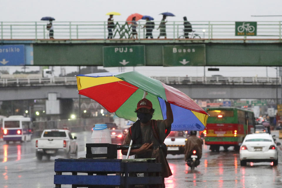 A vendor pushes his cart under an umbrella to shield him from rain from Typhoon Vamco in Quezon city, Philippines on Wednesday, Nov. 11, 2020. Typhoon Vamco blew closer Wednesday to a northeastern Philippine region still struggling to recover from a powerful storm that left a trail of death and destruction just over a week ago, officials said, adding that thousands of villagers were being evacuated again to safety. (AP Photo/Aaron Favila)