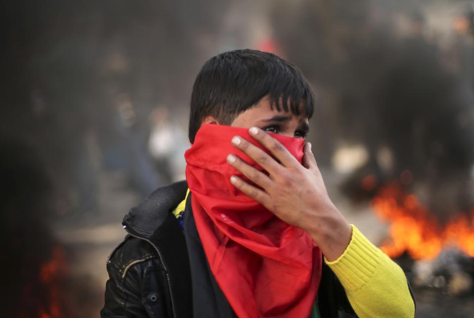 A Palestinian boy stands near burning tyres during a protest against the decision by the main U.N. aid agency to suspend payments to tens of thousands of Palestinians for repairs to their homes damaged in last summer's war, outside the headquarters of the United Nations Special Coordinator in Gaza City January 28, 2015. Dozens of Palestinians, whose homes were destroyed and damaged in the summer war, attacked the office of the United Nations Special Coordinator in Gaza, to protest the decision by a key United Nations organisation to suspend its cash aid to them. Some burnt tyres outside the gate while others tried to storm in by climbing the outer walls. Some hurled stones into the headquarters. REUTERS/Mohammed Salem (GAZA - Tags: POLITICS CIVIL UNREST BUSINESS CONFLICT)