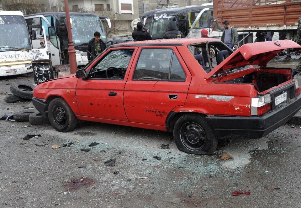 In this photo released by the Syrian official news agency SANA, people inspect the damage to a parking lot at the site of an attack by twin explosions in Damascus, Syria, Saturday, March 11, 2017. Twin explosions Saturday near religious shrines frequented by Shiite pilgrims in the Syrian capital Damascus killed dozens of people, Arab media and activists report. (SANA via AP)