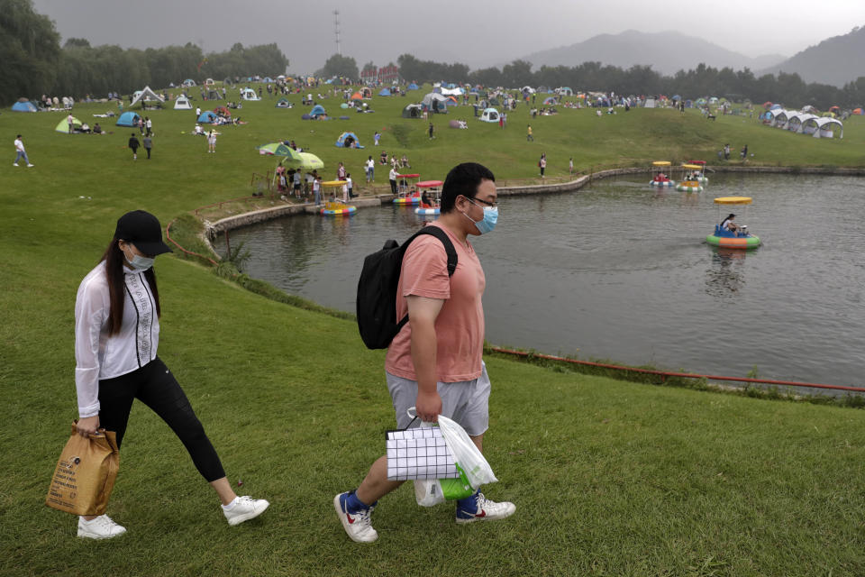 A couple wearing face masks to help curb the spread of the coronavirus walk by people set camp on a scenic mountain in Yanqing, outskirt of Beijing on Sunday, Aug. 30, 2020. China currently has more than 200 people being treated in hospital for COVID-19, with another more than 300 in isolation after testing positive for the virus without displaying symptoms. (AP Photo/Andy Wong)
