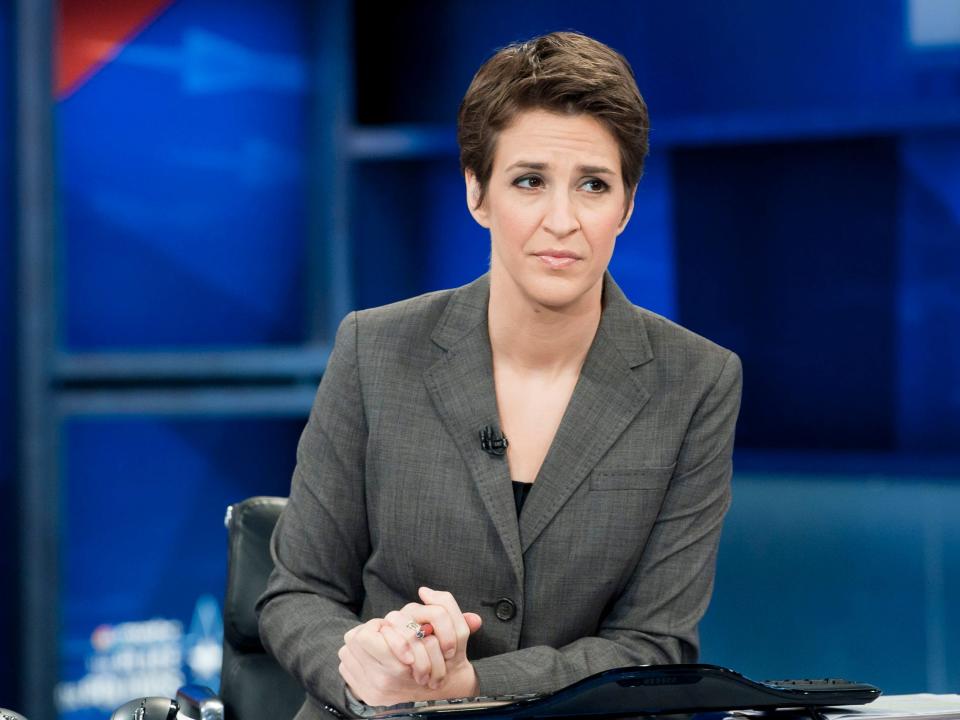 Rachel in a blazer with her hands clasped on a desk.