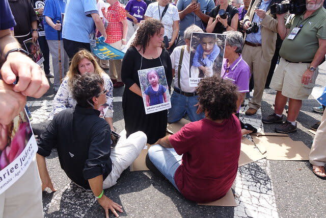 Jacqueline Small,&nbsp;a postulant with the Benedictine Sisters of Erie, kneels on a crosswalk during a Catholic protest in Newark while wearing a photo of&nbsp;Jakelin Caal Maquin, a migrant child who died in detention. (Photo: Ignatian Solidarity Network)