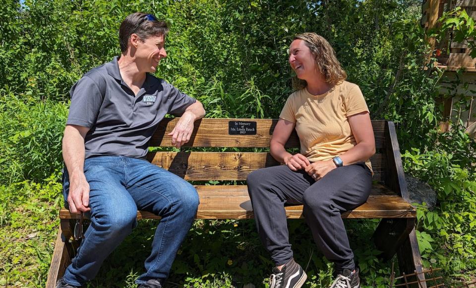 Principal Dave Wood and phys ed teacher Sarah Adams sit on the wooden bench built in honour of Linda Roach in the outdoor classroom. 