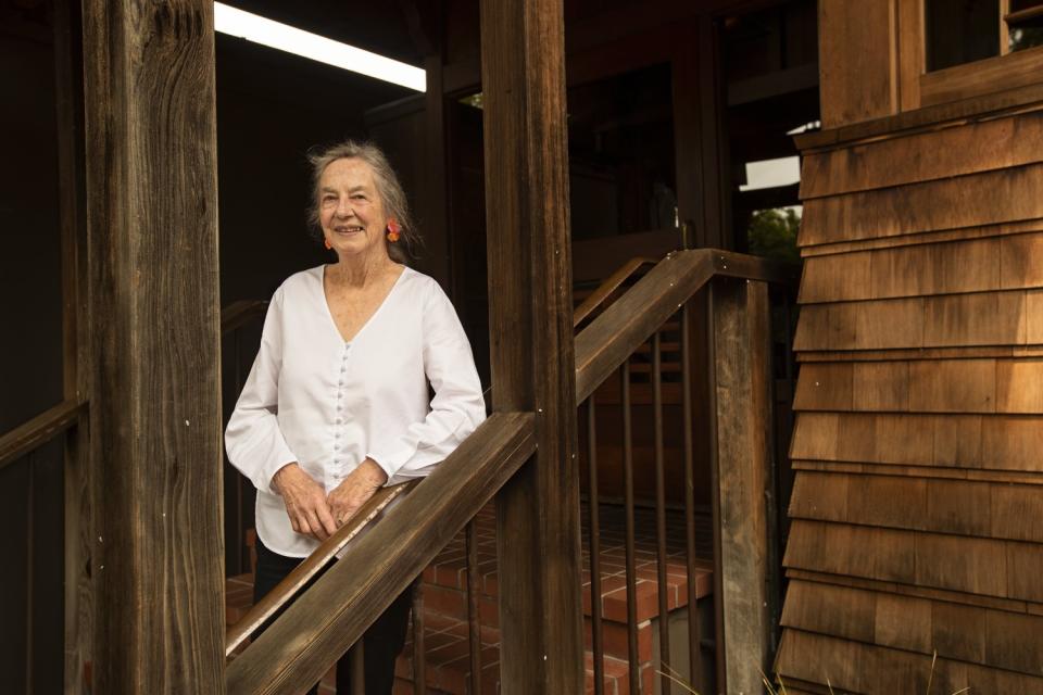 A woman wearing a white blouse leans on a wood banister.