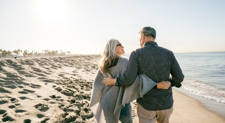A retired couple walks down the beach, arm in arm.