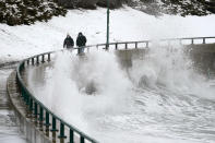 Two men walk along Lynn Shore Reservation as surf kicks up in the aftermath of a snowstorm, Tuesday, Feb. 2, 2021, in Lynn, Mass. A sprawling, lumbering winter storm has walloped the Eastern U.S., shutting down coronavirus vaccination sites, closing schools and halting transit. (AP Photo/Elise Amendola)