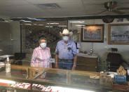 In this photo provided by the Billy The Kid Museum, Lula Sweet, 86, and Don Sweet, 87, pose for a photo behind Plexiglas at the cash register at the Billy The Kid Museum gift shop in Fort Sumner, N.M., in De Baca county, Thursday, July 9, 2020. De Baca is one of two counties in the state where no coronavirus cases have been confirmed. “Most everybody tries to respect each other’s space,” says the Sweets' son, Tim, who runs the museum. (Tim Sweet/Billy The Kid Museum via AP)