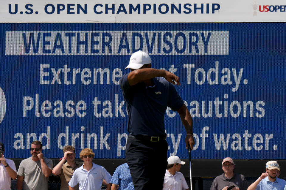 Tiger Woods wipes his face in front of a sign warning of extreme temperatures on the eighth hole during the second round of the U.S. Open golf tournament Friday, June 14, 2024, in Pinehurst, N.C. (AP Photo/Frank Franklin II)