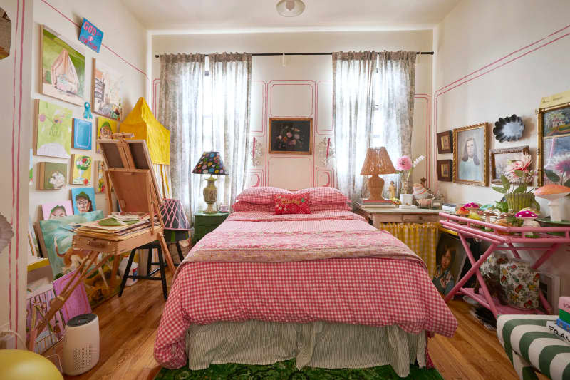 Bed with red bedding and gallery wall with paintings on white walls with trompe l'oeil detail.