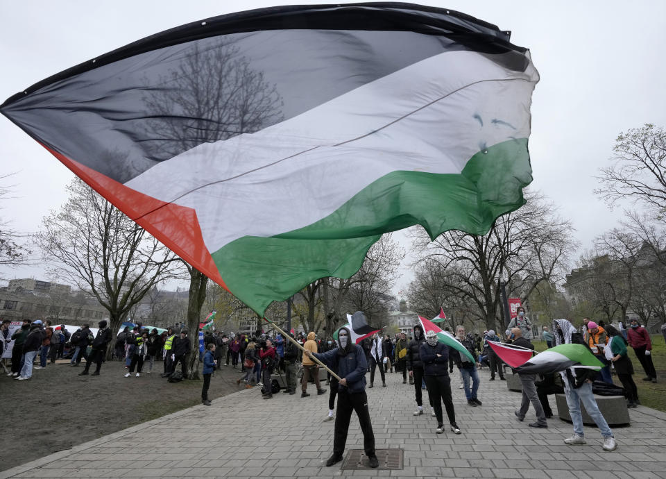 Pro-Palestinian activists wave flags on the outskirts of a protest encampment on the grounds of McGill University, in Montreal, Thursday, May 2, 2024. (Ryan Remiorz/The Canadian Press via AP)
