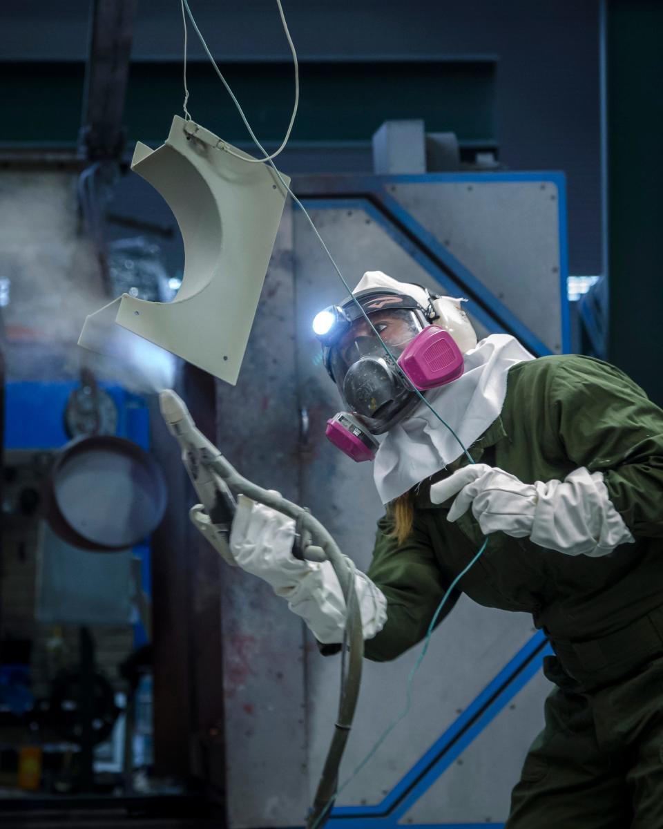Portsmouth Naval Shipyard painter Lynn Mullins powder coats a part in the paint and blast facility.