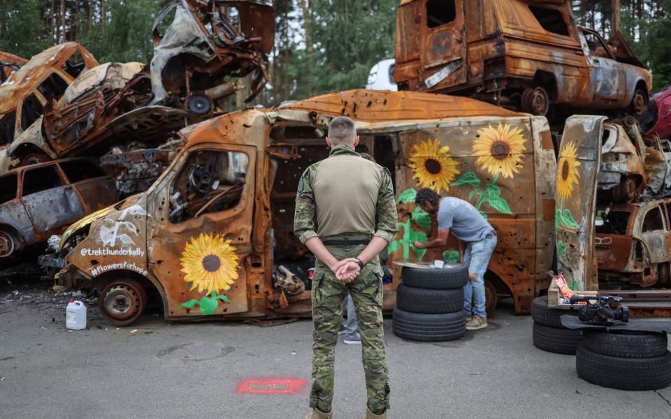 Ukrainian serviceman watches Los Angeles artist Trek Kelly painting a car destroyed a Russian attack in the Kyiv region -  GLEB GARANICH/ REUTERS