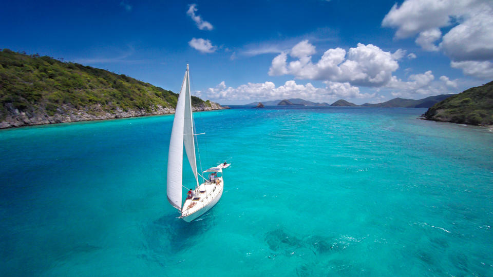 aerial view of a sloop under full sails sailing through the Caribbean.