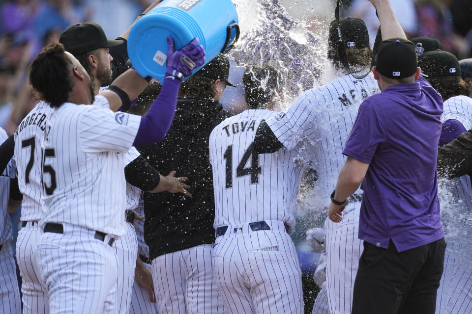 Colorado Rockies catcher Elias Díaz, far left, dumps water onto teammates as they mob Ryan McMahon, who crosses home plate after hitting a grand slam off Tampa Bay Rays pitcher Jason Adam during the ninth inning of a baseball game Friday, April 5, 2024, in Denver. (AP Photo/David Zalubowski)