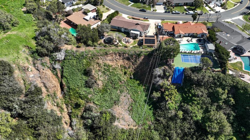 Aerial view of a neighborhood of homes, roads and sloping land nearby.