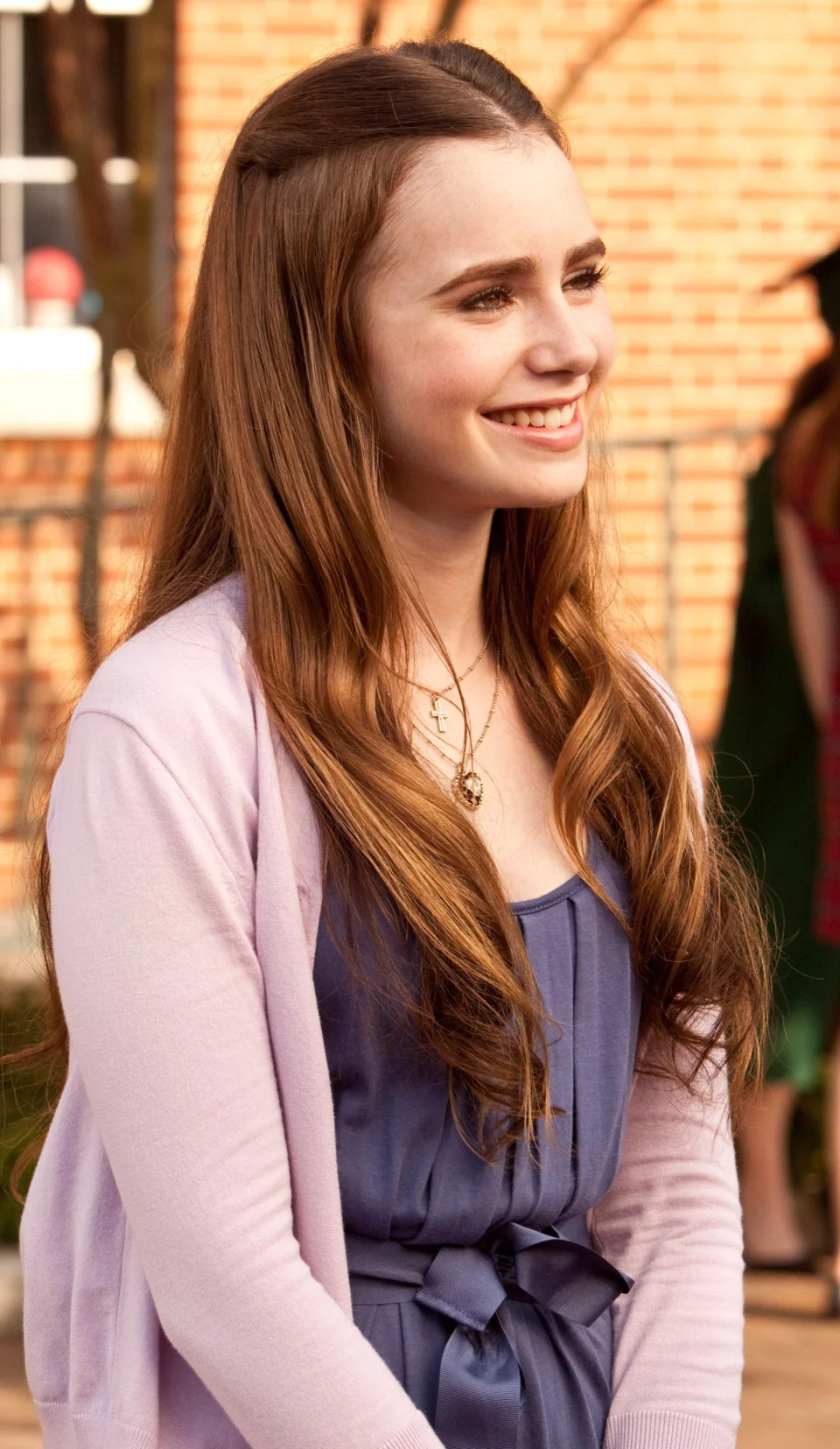 Lily Collins stands outdoors, smiling in a casual outfit in "The Blind Side"