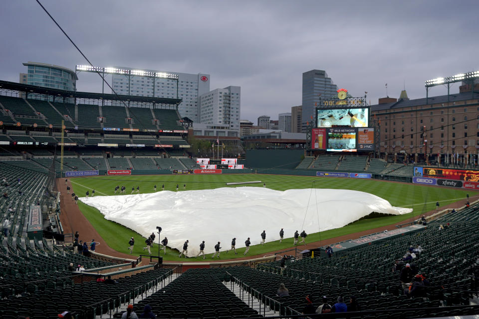 Grounds crew members place a tarp over the infield at Oriole Park at Camden Yards prior to a baseball game between the Baltimore Orioles and the Seattle Mariners, Monday, April 12, 2021, in Baltimore. (AP Photo/Julio Cortez)