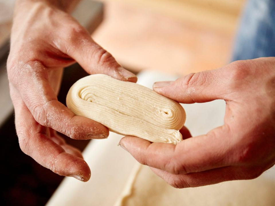 Man holding folded dough in the kitchen.