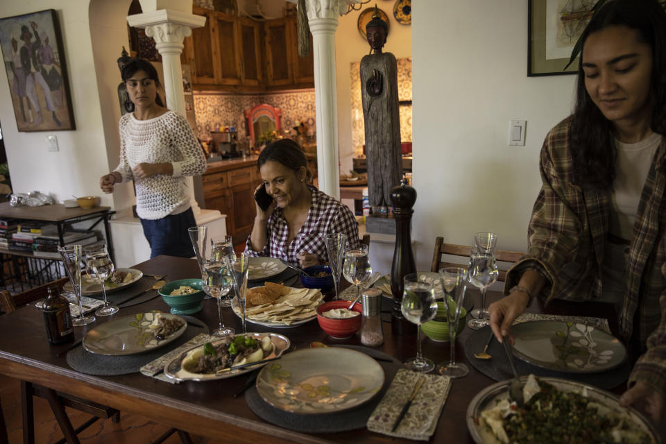 La empresaria Youri Mevs habla por su celular sentada a la mesa con sus hijas, en su casa en Puerto Príncipe, Haití. el 29 de septiembre de 2021. Quiere que sus hijas pasen a formar parte del grupo de quienes se van en tanto se decide qué sucede con Haití. Si la situación no mejora, ella también podría tener que vender sus empresas e irse. (AP Foto/Rodrigo Abd)