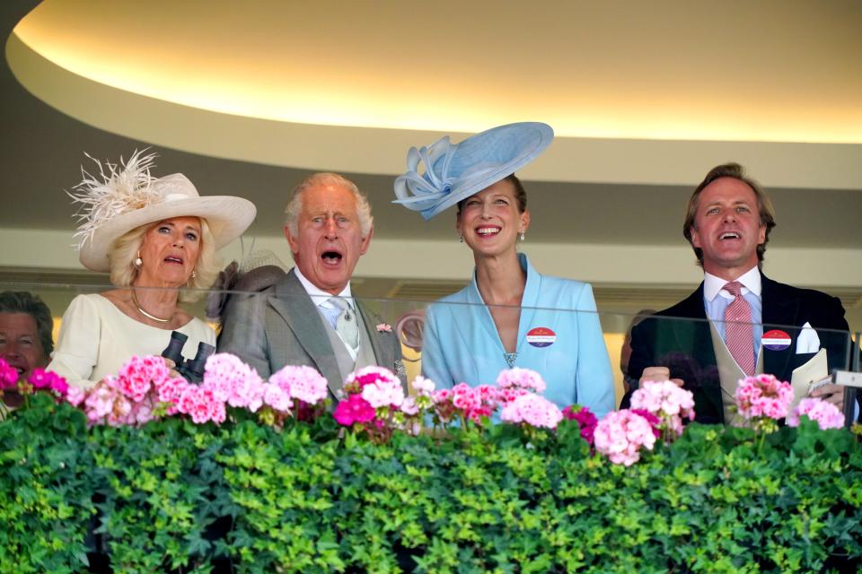 Charles, Camilla, Lady Gabriella Kingston, and Thomas Kingston exclaiming together while standing at a glass balcony lined with pink flowers.