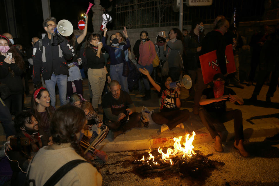 Manifestantes israelíes bloquean un camino durante una protesta en demanda del primer ministro israelí Benjamín Netanyahu, cerca de su residencia oficial en Jerusalén, durante la tercera jornada nacional de confinamiento por el coronavirus, el sábado 2 de enero de 2021. (AP Foto/Ariel Schalit)