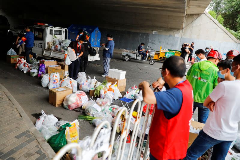 People deliver food near a barrier that was placed around a residential compound that is under lockdown in the Fengtai district, in Beijing