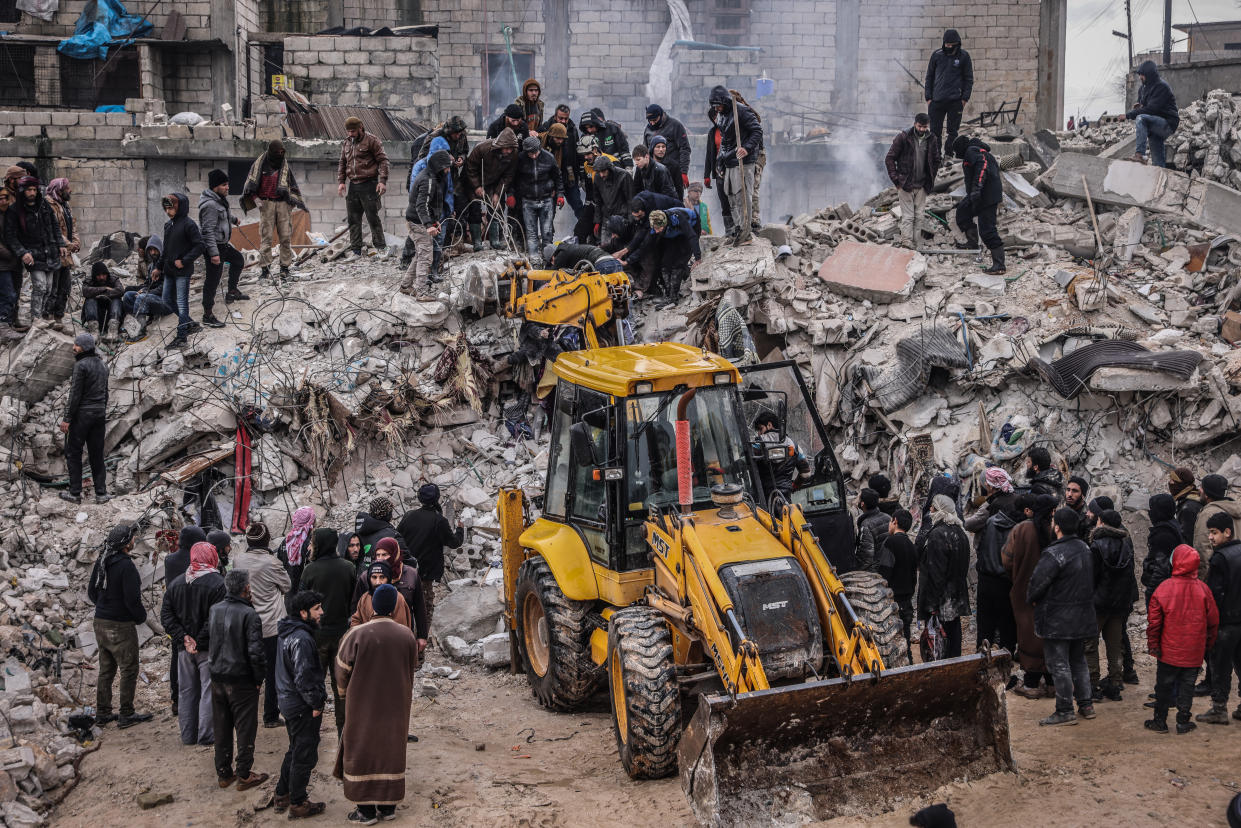 Rescue workers and civilians conduct search-and-rescue operations in the rubble of a collapsed building.