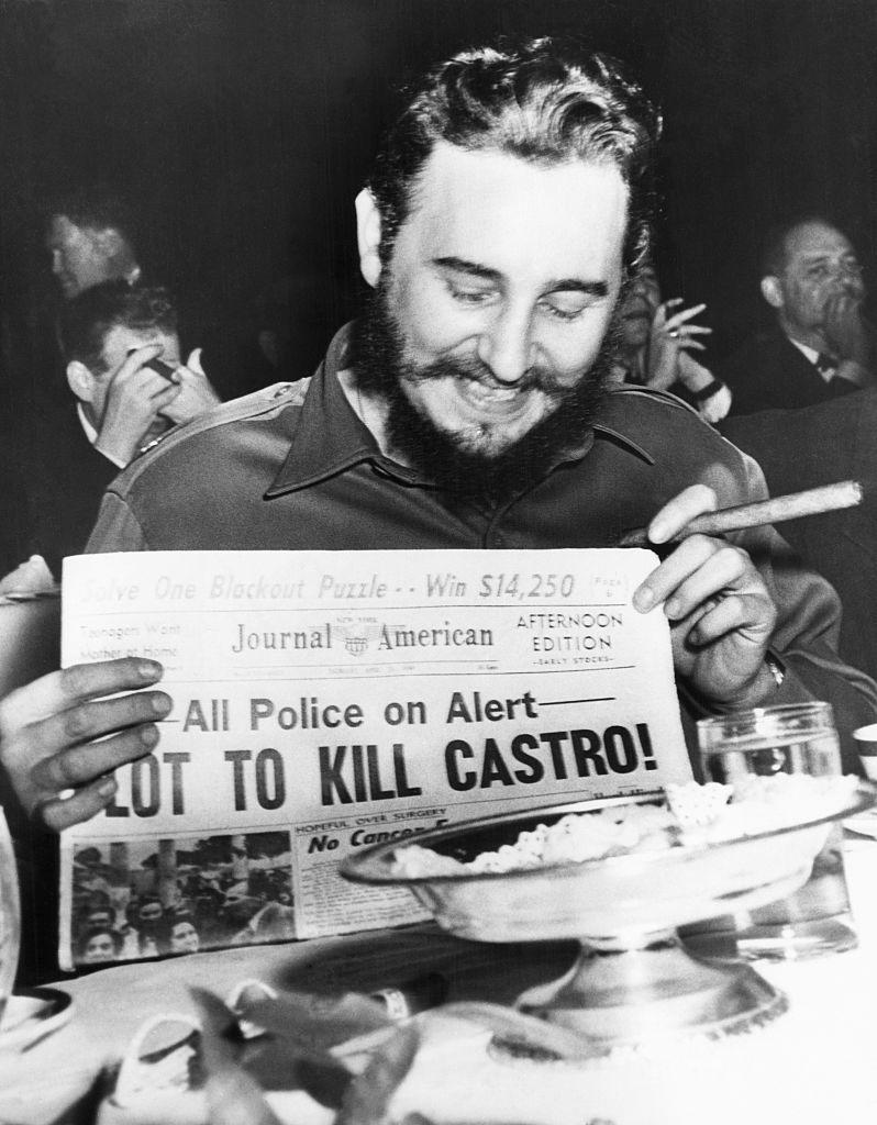 Castro smiling and holding a newspaper with headline "Plot to Kill Castro"
