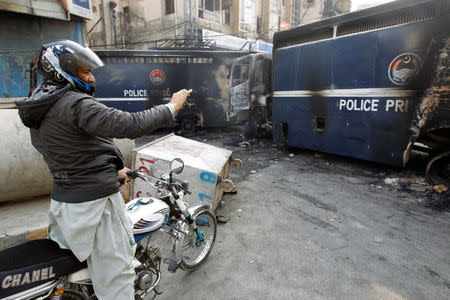 A passerby photographs police prison vans destroyed during clashes with protesters near the Faizabad junction in Islamabad, Pakistan November 26, 2017. REUTERS/Caren Firouz