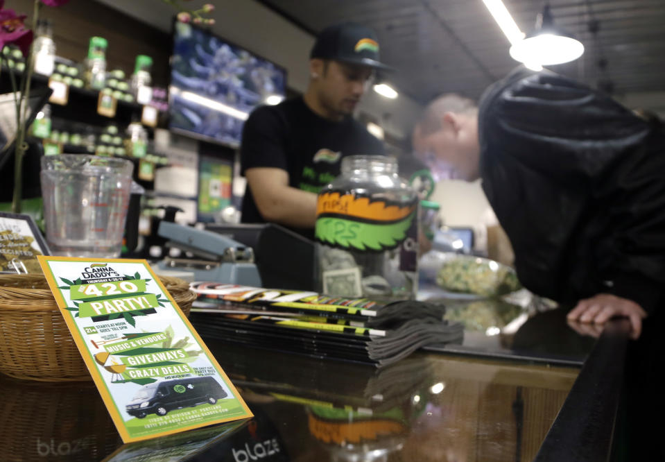 FILE - In this April 20, 2017, file photo, a cannabis dispensary customer, right, smells a marijuana sample from a budtender at CannaDaddy's Wellness Center marijuana dispensary in Portland, Ore. In Oregon, cannabis retailers saw a huge spike in March 2020, a 30% increase in average sales per retailer compared with March 2019. Sales increases mid-month were even larger. However, the peak has leveled off and customers are coming in less frequently but buying more, said David Alport, who owns two Bridge City Collective stores in Portland. (AP Photo/Don Ryan, File)