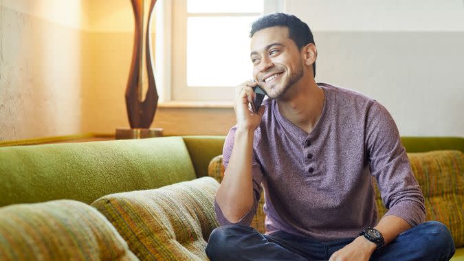 Smiling young man answering smart phone on couch.