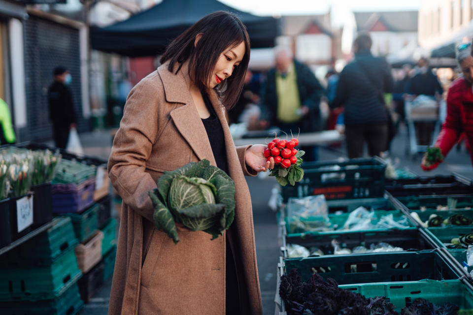 Young Asian woman shopping for fresh organic vegetables at local farmer market. Putting a cabbage and raddish into an eco-friendly cotton mesh shopping bag. Zero waste concept. Local businesses idea. Local food market.