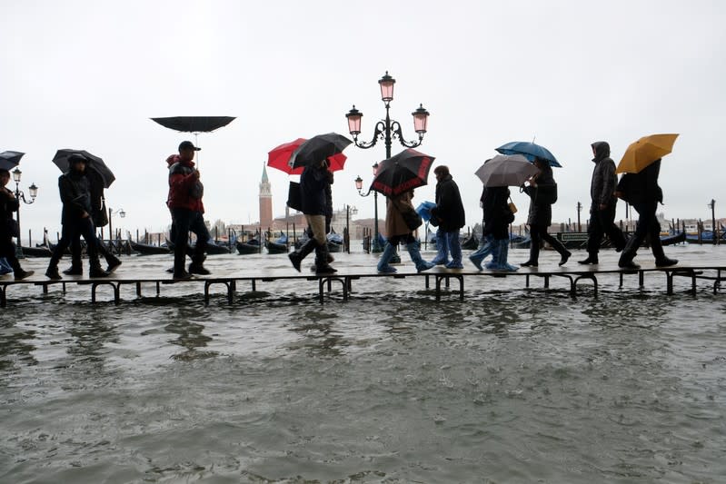 People walk on a catwalk in the flooded St.Mark's Square during a period of seasonal high water in Venice