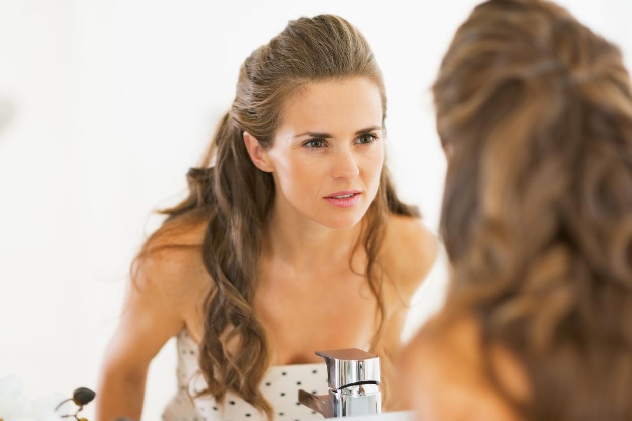 concerned young woman looking in mirror