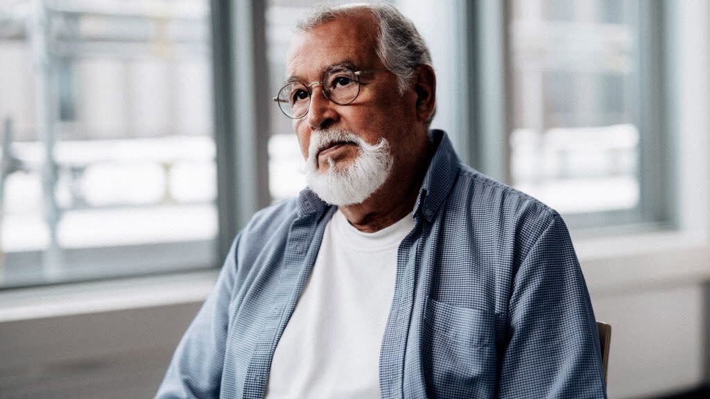 An older man with gray hair and wearing glasses sits inside a doctor's office