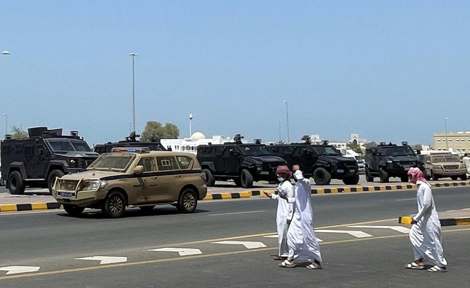 People walk near riot police cars in Sohar, Oman, Tuesday, May 25, 2021. On Tuesday, dozens of protesters angry over firings and the poor economy of Oman marched in Sohar, a city some 200 kilometers northwest of the capital, marking a third day of demonstrations in the typically subdued sultanate. (AP Photo)