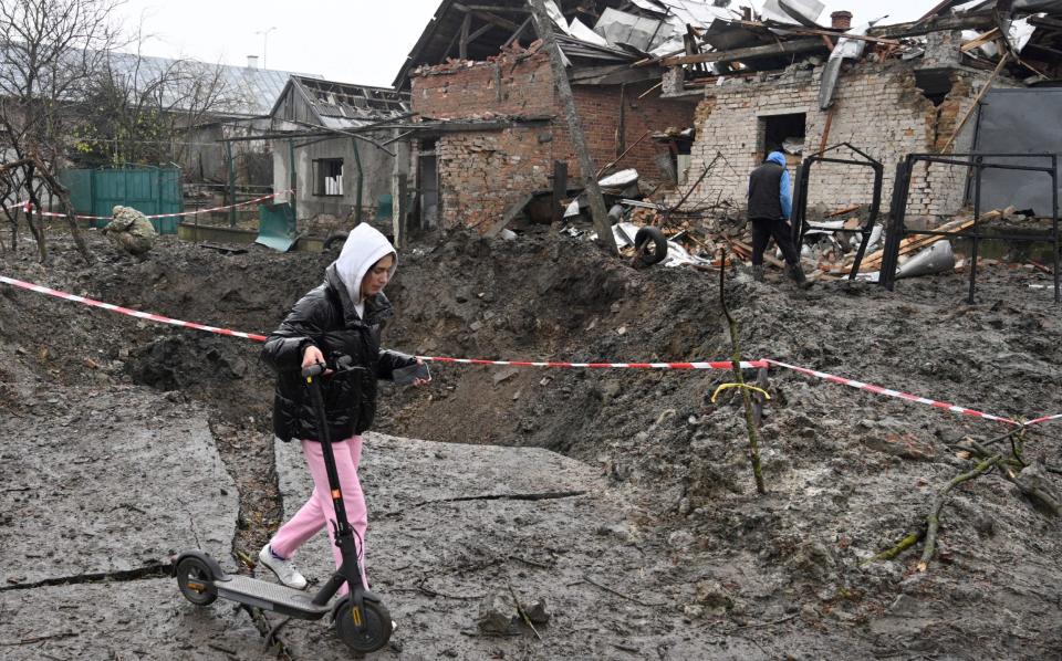 A girl carries a kick scooter as she walks past a crater after a missile strike in a village, near the western Ukrainian city of Lviv - YURIY DYACHYSHYN / AFP