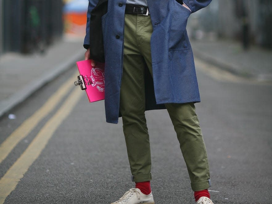 man wearing a long blue trench coat over a sweater and green chinos
