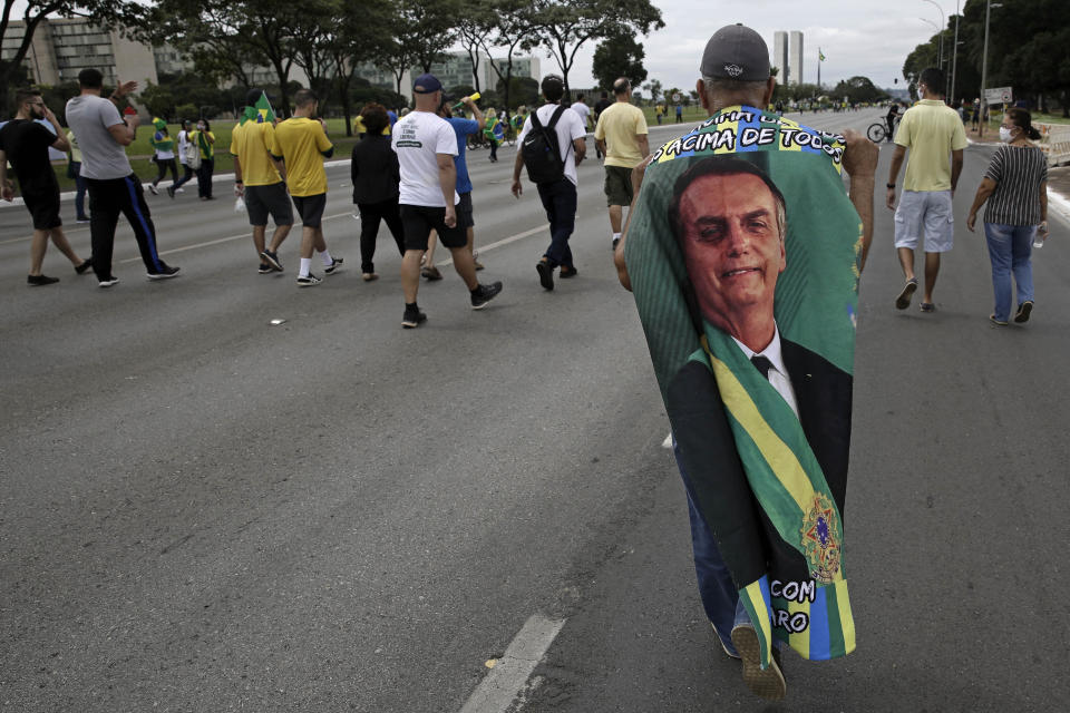 A demonstrator, wearing a cape emblazoned with an image of President Jair Bolsonaro, walks with others to the National Congress, as part of a caravan backing Bolsonaro’s anti-coronavirus-lockdown stance, marking May Day, or International Workers' Day, in Brasilia, Brazil, Saturday, May 1, 2021. (AP Photo/Eraldo Peres)