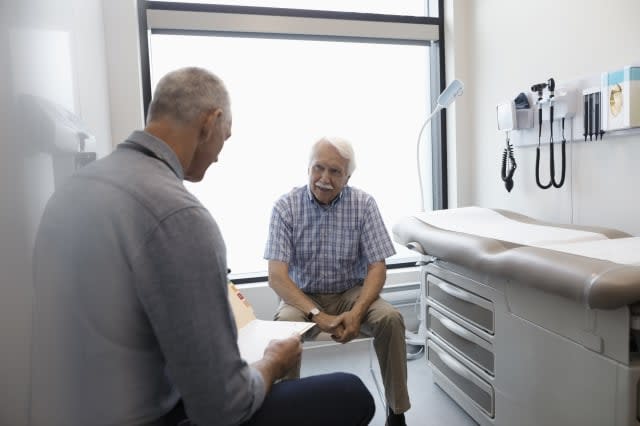 Male doctor discussing medical record with senior patient in clinic exam room